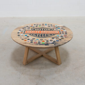 Round wooden coffee table with harley-davidson logo in the middle, with 108 harley poker chips from dealers around the world, around the logo.