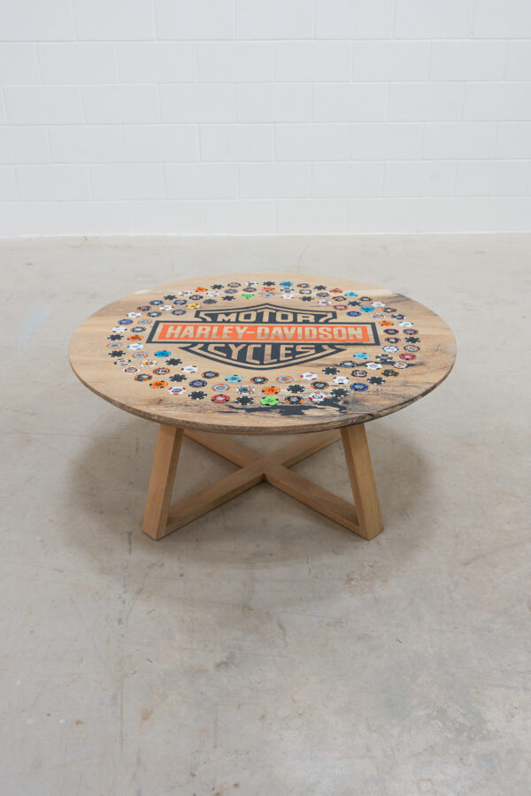 Round wooden coffee table with harley-davidson logo in the middle, with 108 harley poker chips from dealers around the world, around the logo.